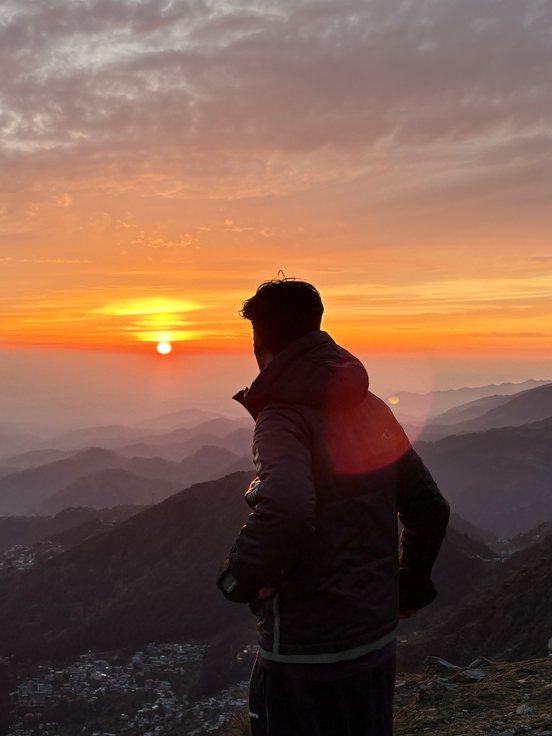 Chirag on a hilltop, looking out at the sunset over the hills